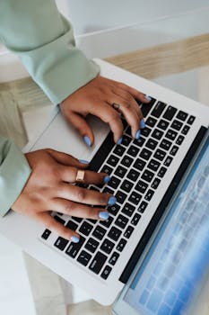 A person typing on a laptop with blue nail polish, showcasing modern technology.