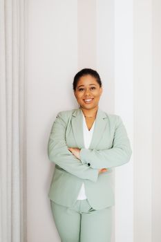 一位穿着商务服装的非裔美国妇女面带微笑，双臂交叉站在室内