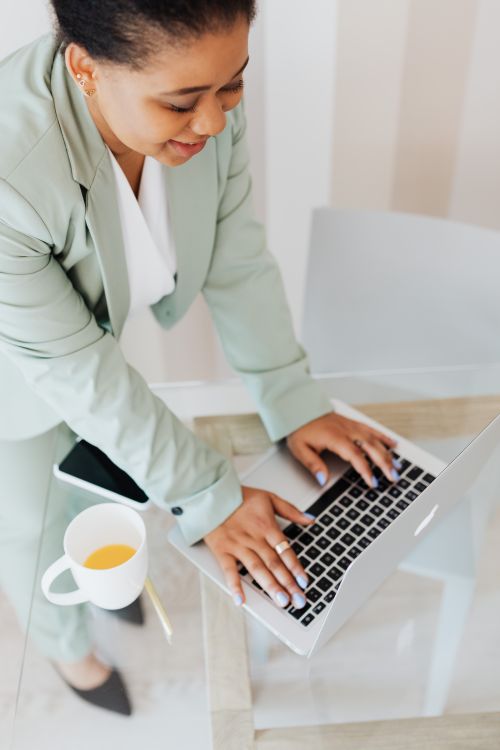 Free Businesswoman in a suit working on a laptop at a glass desk with coffee. Stock Photo