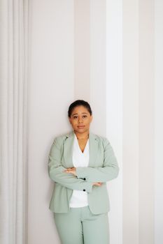 一位自信的女人身穿薄荷绿色西装，双臂交叉，站在白色背景前