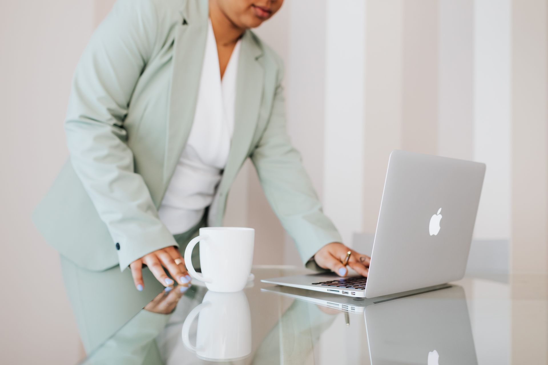 Business professional using a laptop in a modern office environment with a cup of coffee on a glass table.