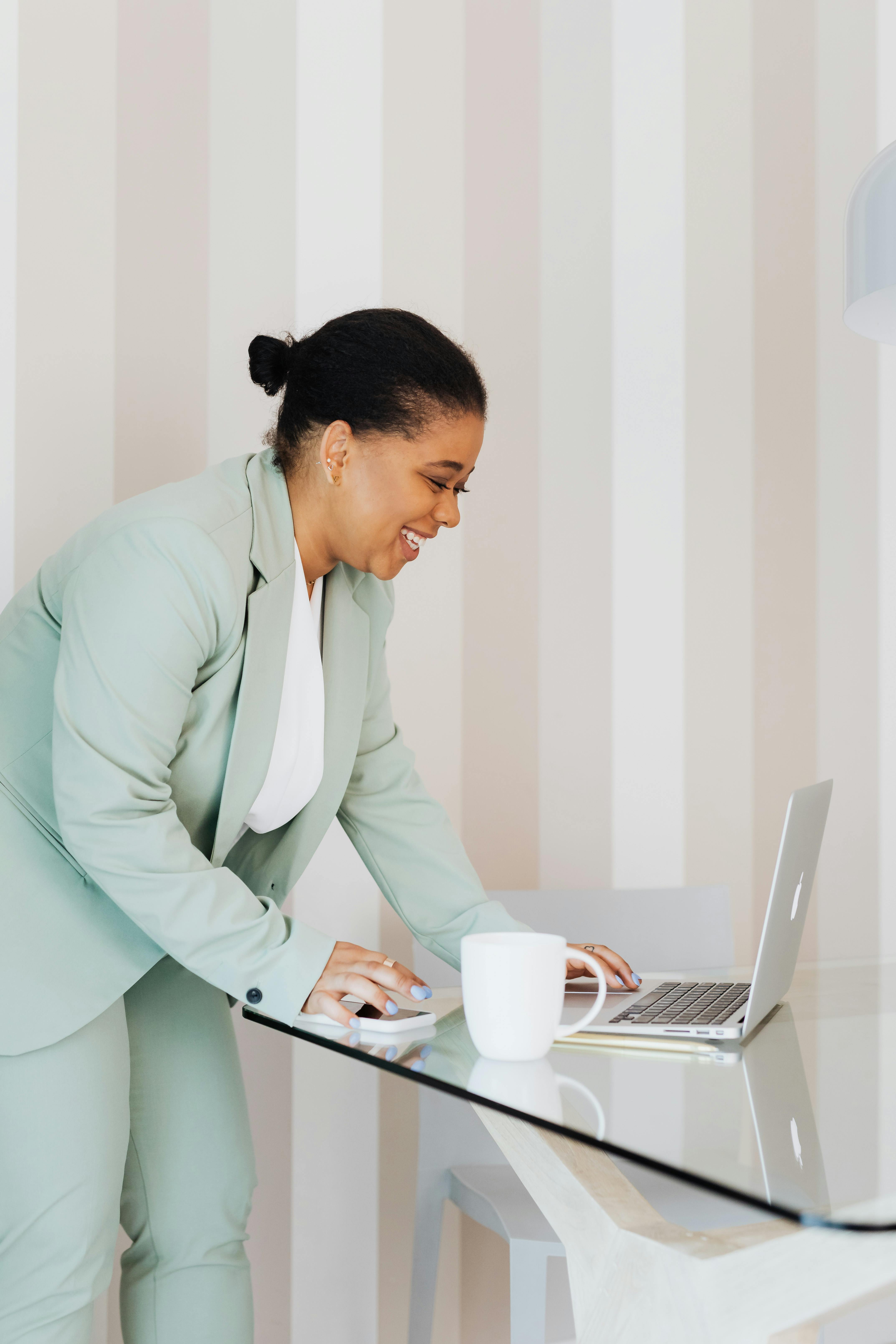 一位穿着正式服装的自信女人，在室内玻璃桌旁使用笔记本电脑时微笑着