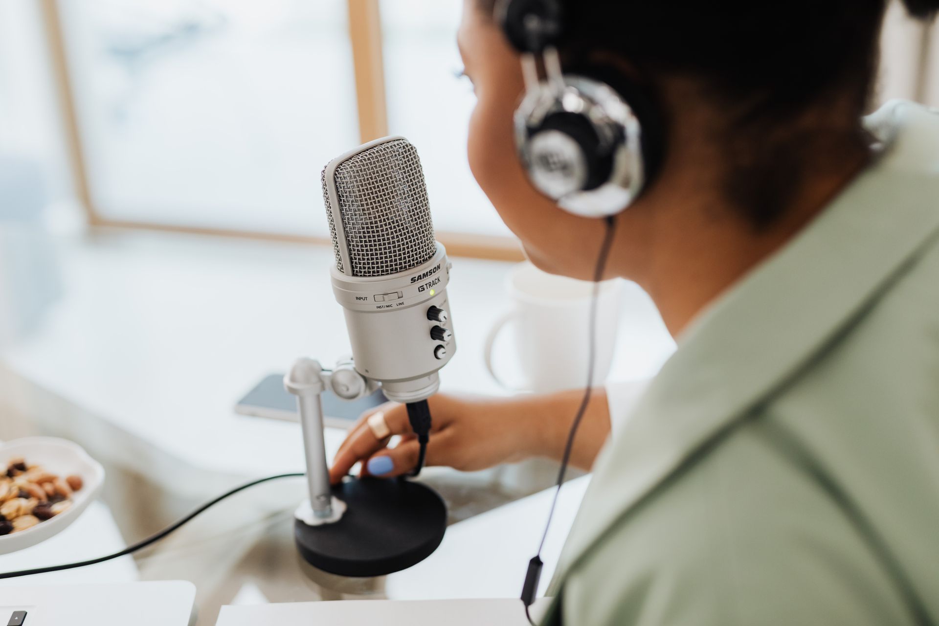 Woman using a microphone and headphones indoors, focusing on recording a podcast or voiceover.