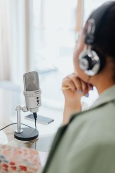 A woman with headphones and microphone, recording in a bright home studio.