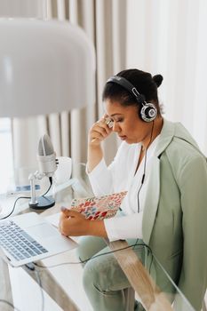 Professional woman in home office setup recording a podcast with headphones, laptop, and microphone.