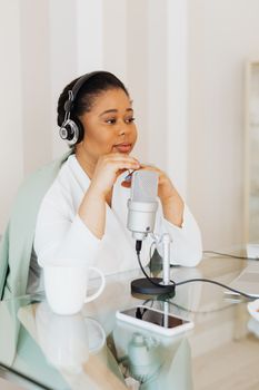 Woman wearing headphones, using a microphone while podcasting at a glass table.