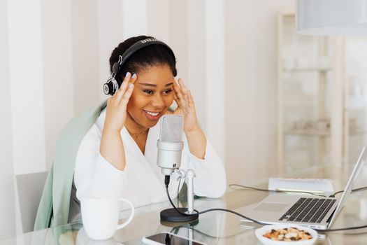 Woman in a home studio recording a podcast with a laptop and microphone.