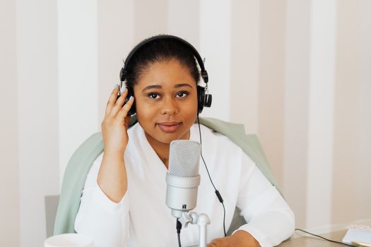 Young woman podcaster with headphones at a desk using a microphone.