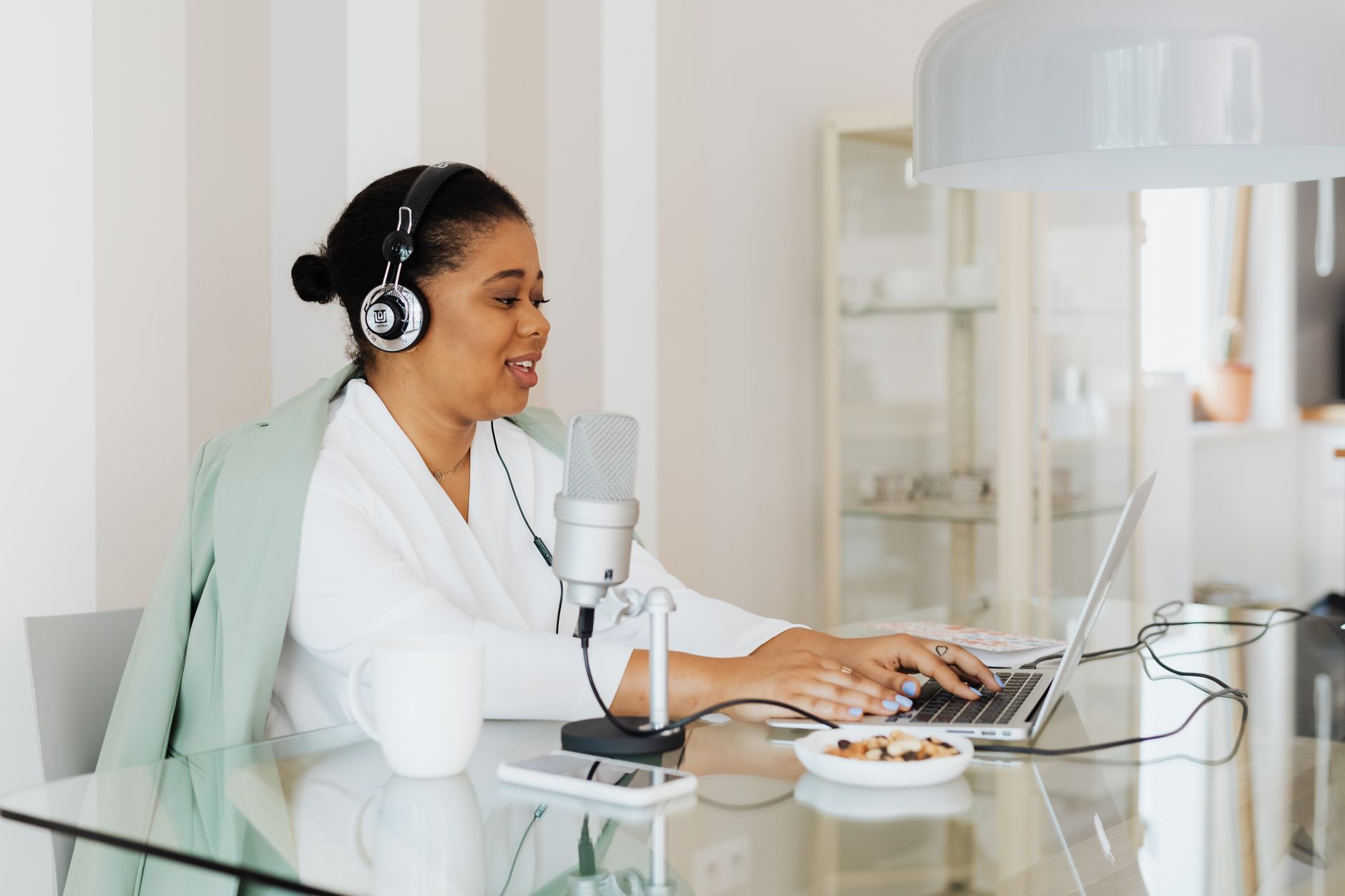Woman podcasting with microphone and laptop in a contemporary office setting.