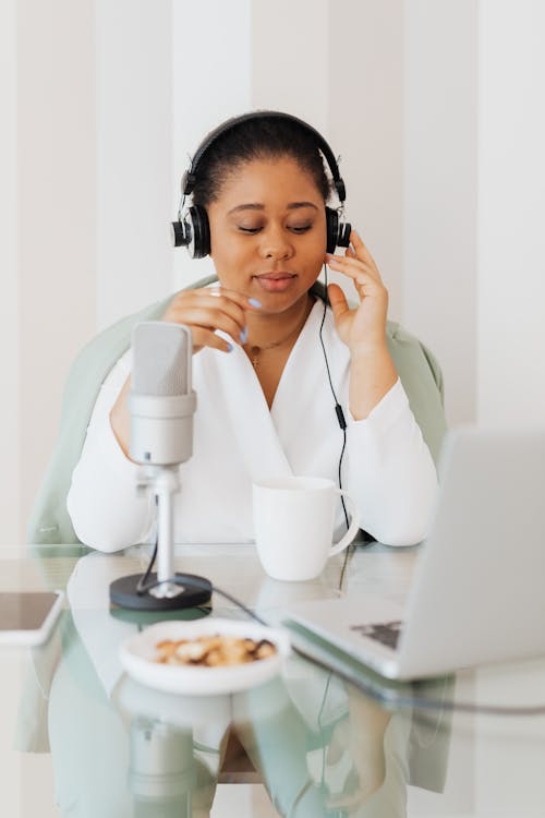 Woman Sitting Behind a Glass Desk with Headphones On and Using a Laptop 