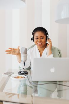 Woman in professional setting recording with a microphone and laptop for a podcast or online meeting.