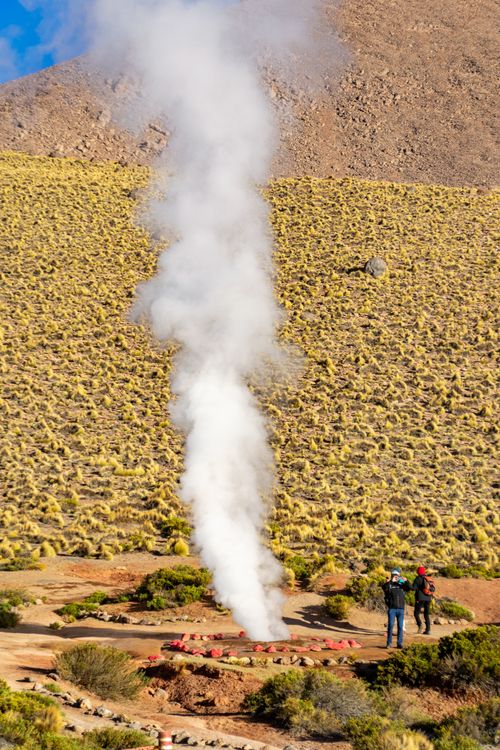 Free A stunning view of a geyser eruption with two onlookers in Chile's Andes Mountains. Stock Photo
