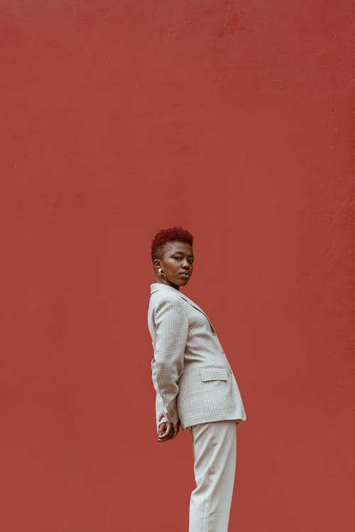 Young pensive serious African American female in white suit leaning back and looking at camera on red background