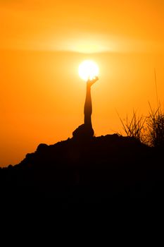 Silhouette of unrecognizable male lying on hill with raised hand to sun against bright sundown sky