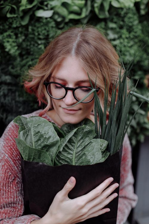 Free Woman with glasses hugging lush green leaves in a cozy setting. Stock Photo