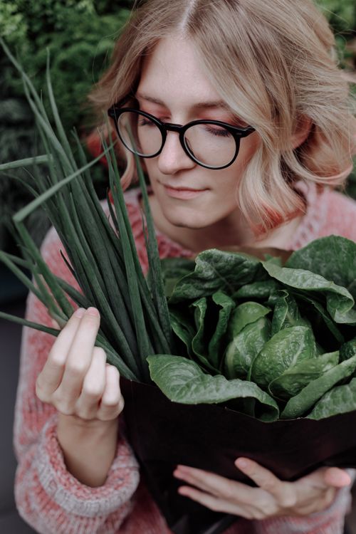 Free A woman in eyeglasses holds fresh leafy vegetables, showcasing organic produce. Stock Photo
