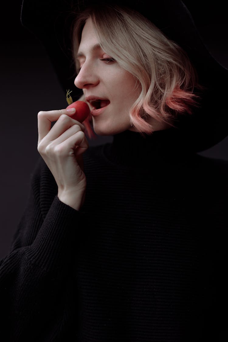 Woman In Black Long Sleeve Shirt Eating A Red Vegetable