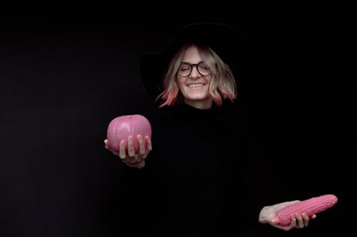 A Woman in Black Clothes Holding a Pink Pumpkin and a Pink Corn