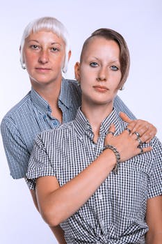 Close-up portrait of two stylish women in plaid shirts, showcasing unique hairstyles and jewelry.