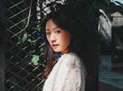 Woman in White Long Sleeve Shirt Standing Beside Green Plant