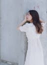Woman in White Dress Leaning on Gray Wall