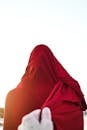 Faceless person pulling edge of red cloth wrapping faceless person standing against cloudless blue sky