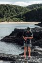Man in Black T-shirt and Blue Denim Shorts Standing on Rock Near Body of Water