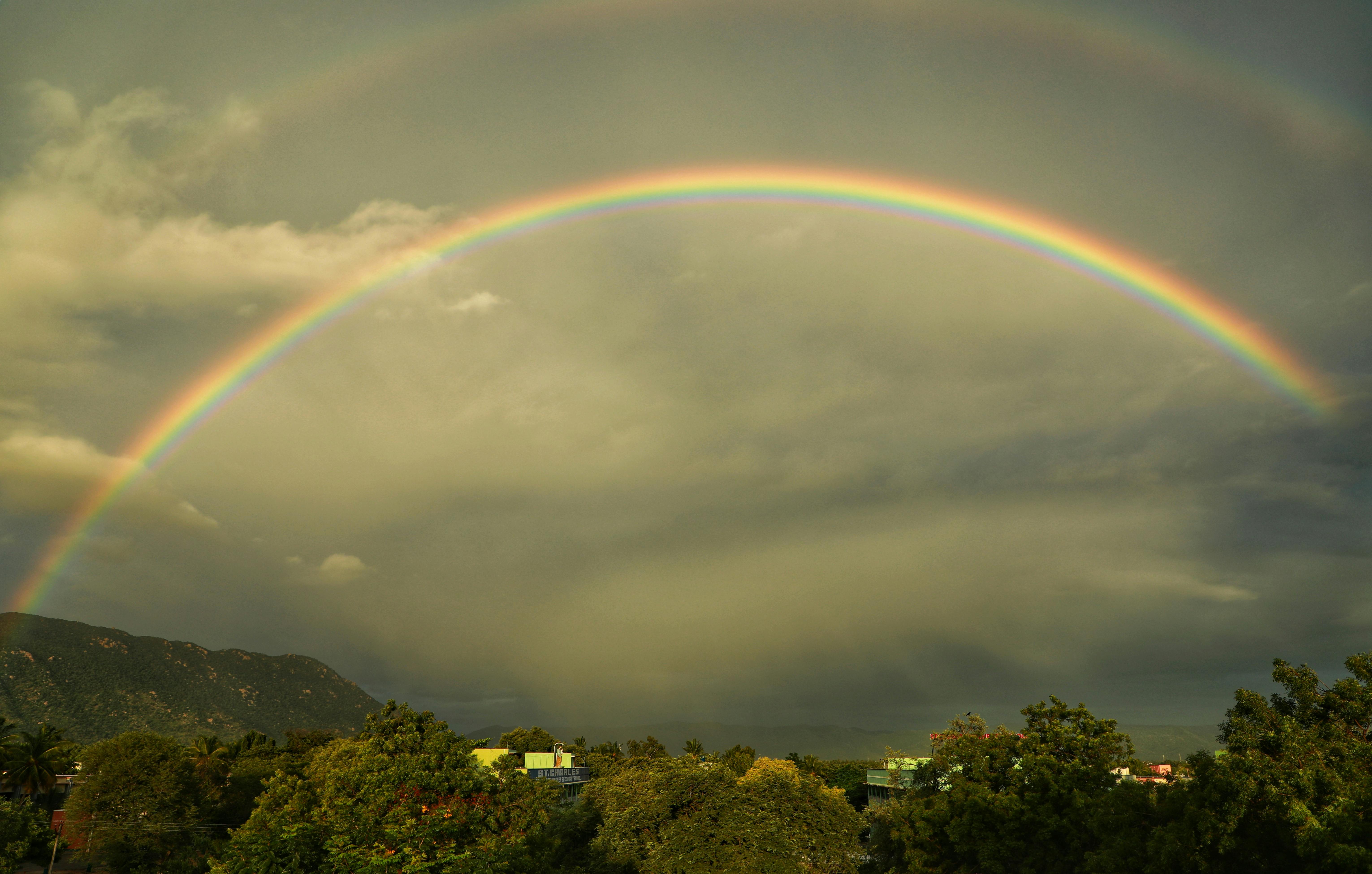 一道充满活力的彩虹弧划过风景秀丽的山谷，山谷中遍布郁郁葱葱的绿色植物，上空是戏剧性的云层
