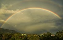 一道充满活力的彩虹弧划过风景秀丽的山谷，山谷中遍布郁郁葱葱的绿色植物，上空是戏剧性的云层