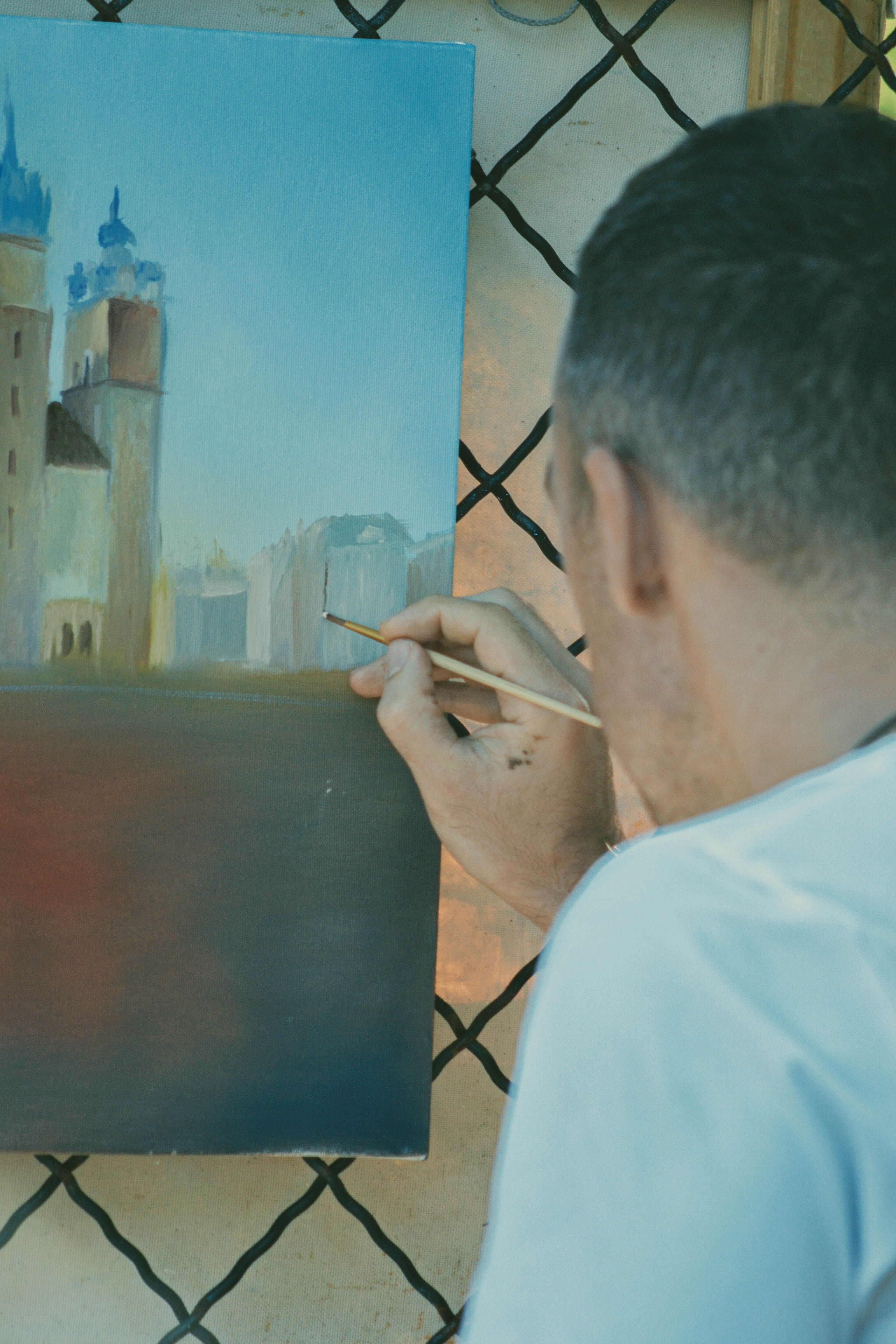 A man skillfully painting an urban cityscape with a brush on canvas outdoors.