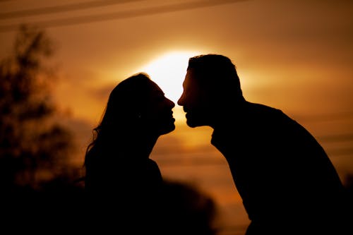 Side view silhouettes of unrecognizable happy man and woman smiling and looking at each other during date against sunset sky