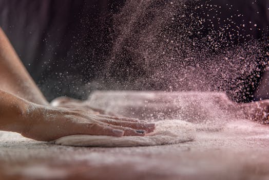 Hands kneading dough with flour dusting in the air, capturing the art of baking.