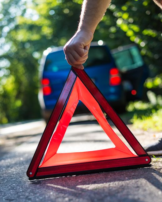 A driver placing a reflective warning triangle on the road beside a stopped car