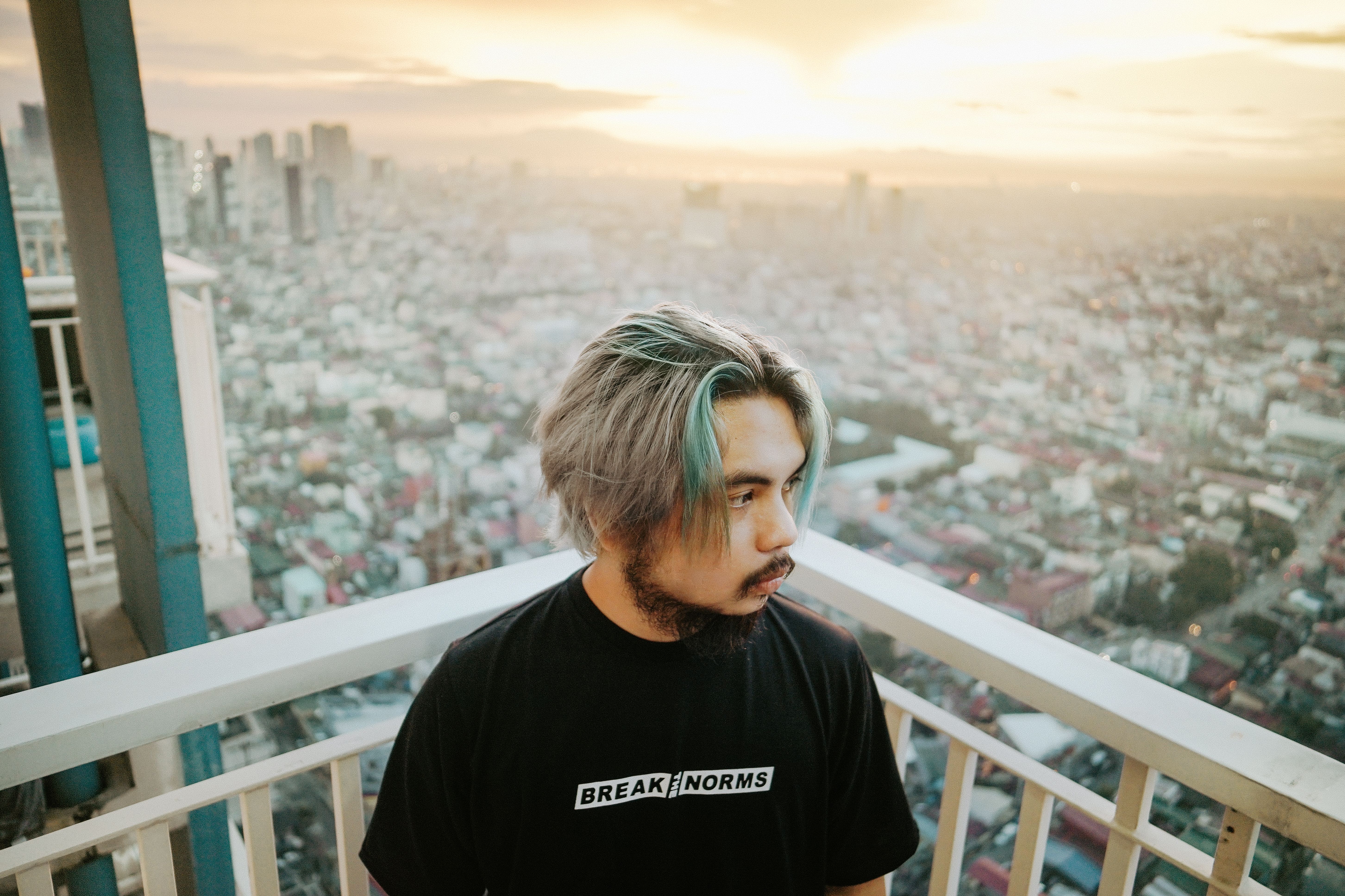 一个留着独特发型、身穿街头服饰的男人，在日落时分俯瞰着充满活力的马尼拉天际线