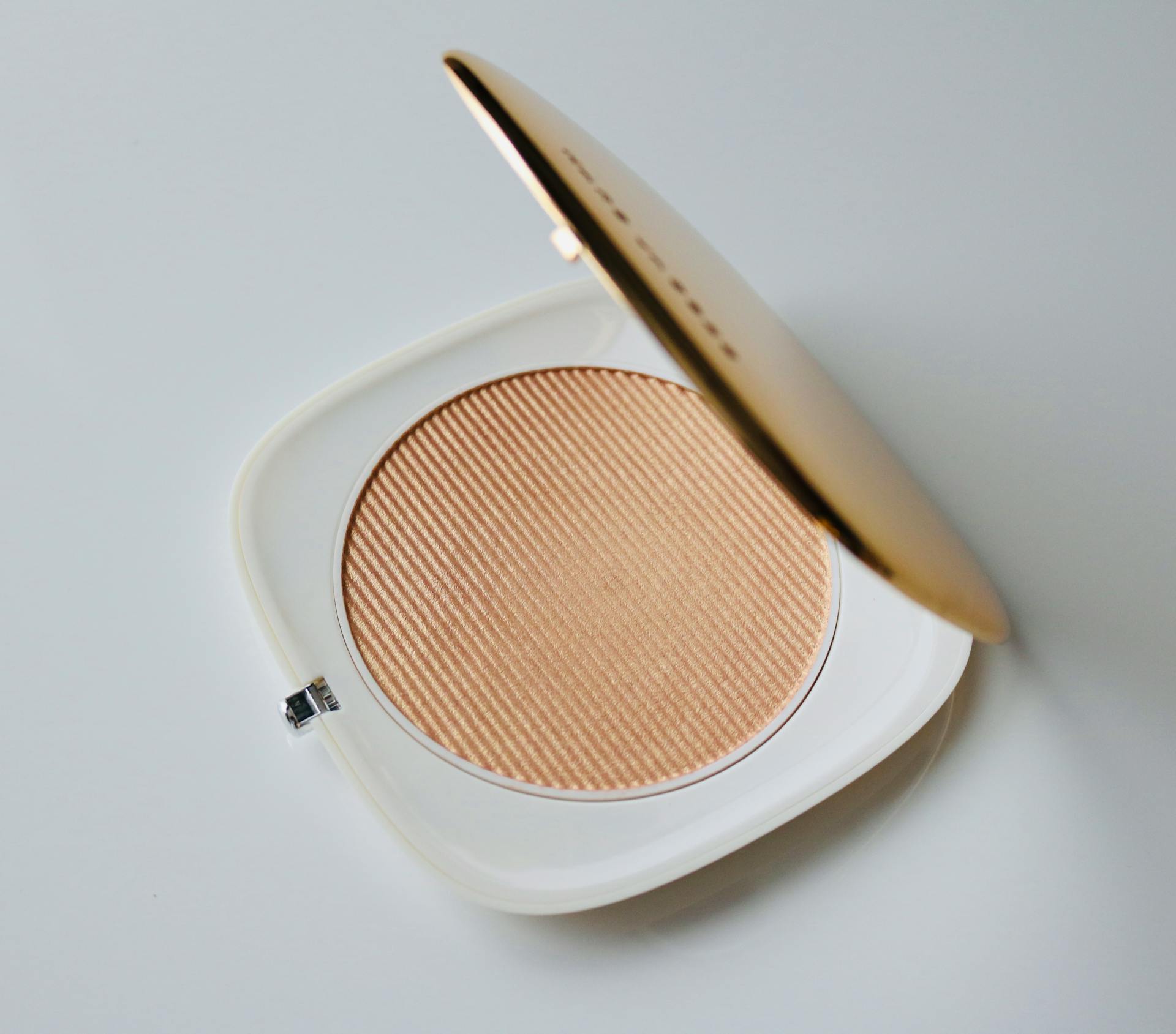 Minimalist photo of a compact powder in an elegant white container with mirror lid.