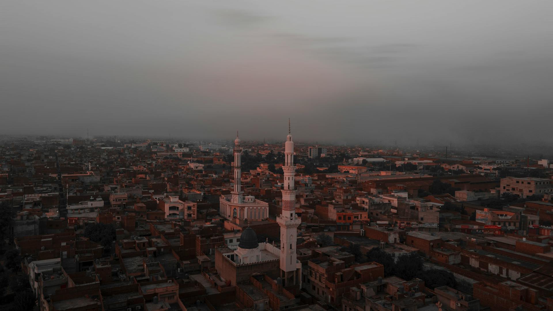 Dramatic aerial view of Gujranwala cityscapes with minarets under a moody dusk sky.