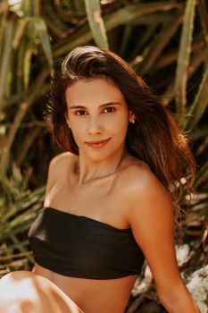Young attractive female in beachwear with long hair sitting on beach and looking at camera