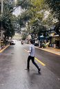 在成都，一个人穿过一条潮湿的街道，头顶是郁郁葱葱的树冠