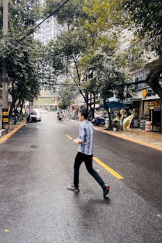 在成都，一个人穿过一条潮湿的街道，头顶是郁郁葱葱的树冠