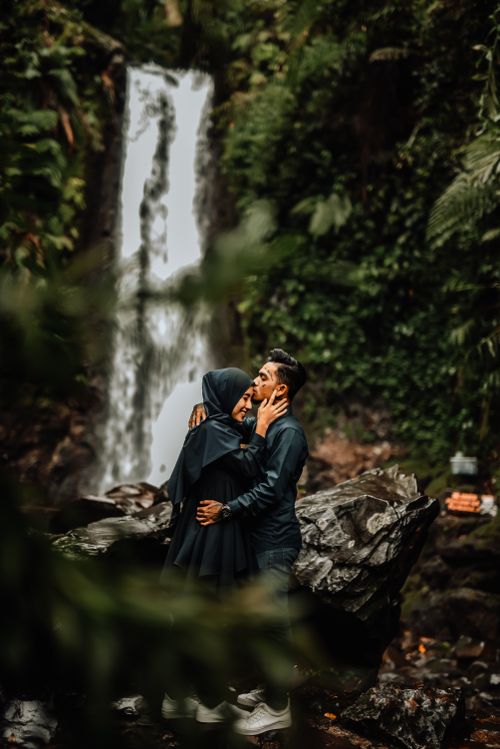 Free A couple shares an intimate moment by a lush waterfall, symbolizing love and nature's beauty. Stock Photo