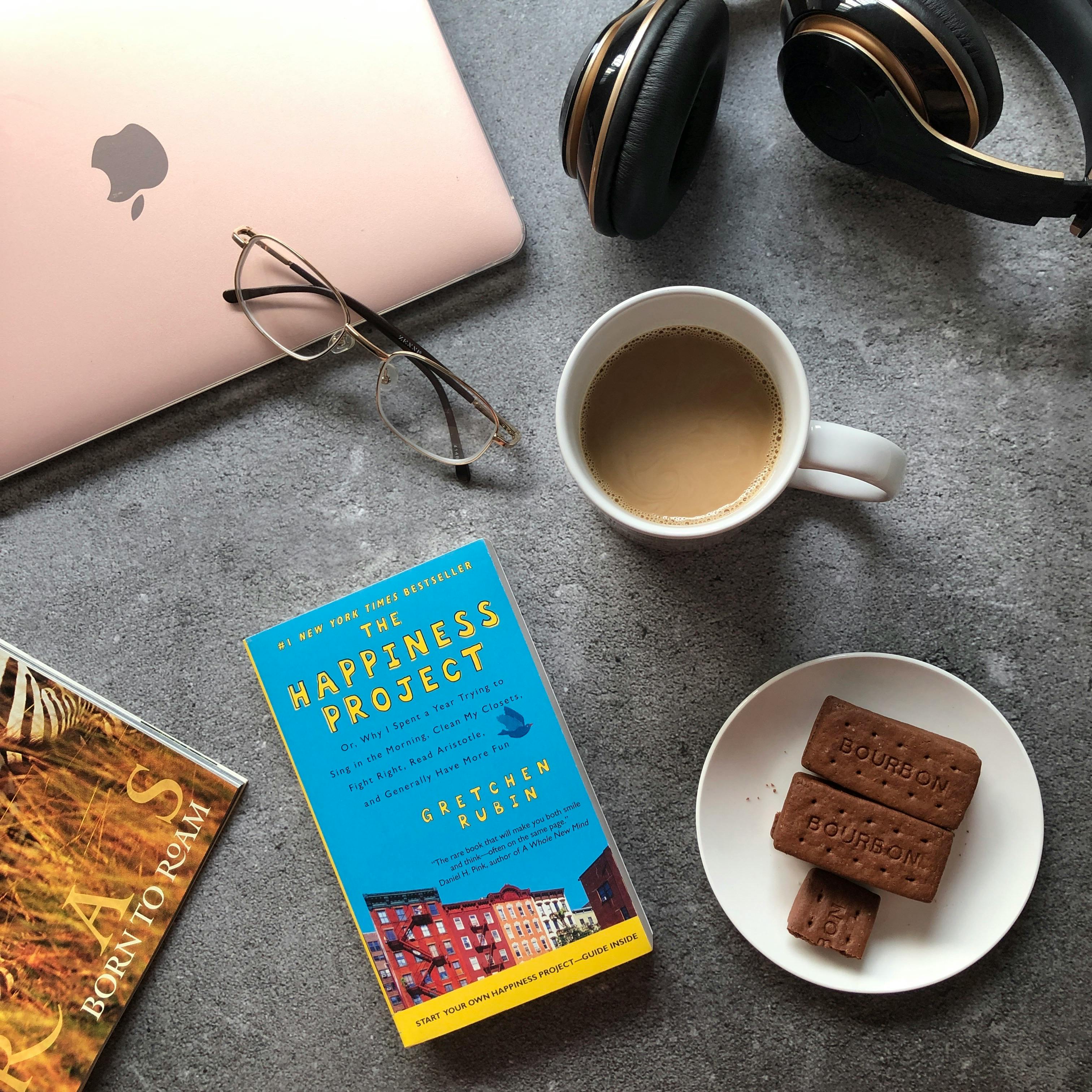 Flat lay of coffee, books, headphones, and treats on a desk.
