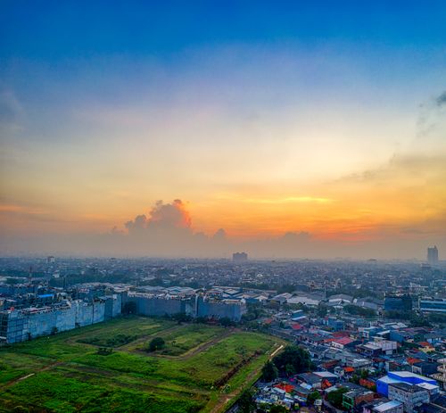 Free Aerial view of Jakarta's skyline during sunset with green fields and distant buildings. Stock Photo