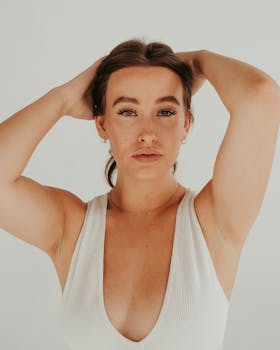 一位身穿白色背心的女人，双手放在头上，背景平淡的特写肖像
