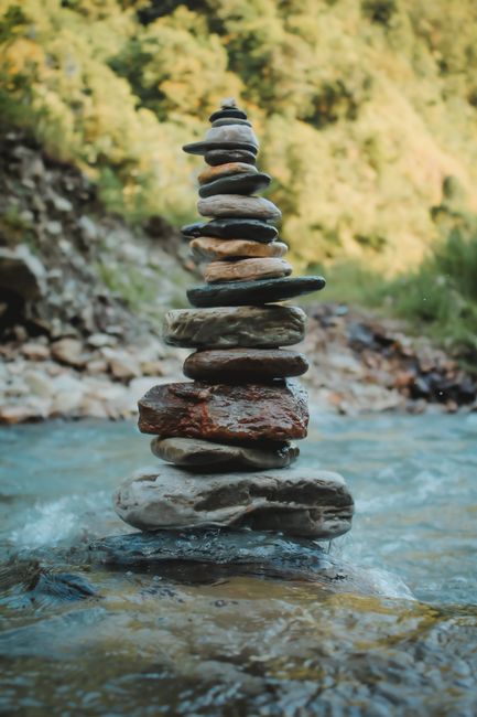 Fotomural Una pila equilibrada de piedras junto a un río fluyente en medio de una vegetación exuberante.