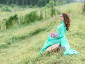 Woman in a Green Dress Holding a Bunch of Flowers Sitting on a Field 