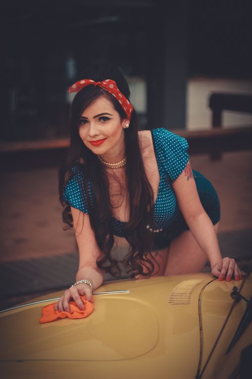 Free Smiling woman in retro attire cleaning a vintage yellow car outdoors. Stock Photo