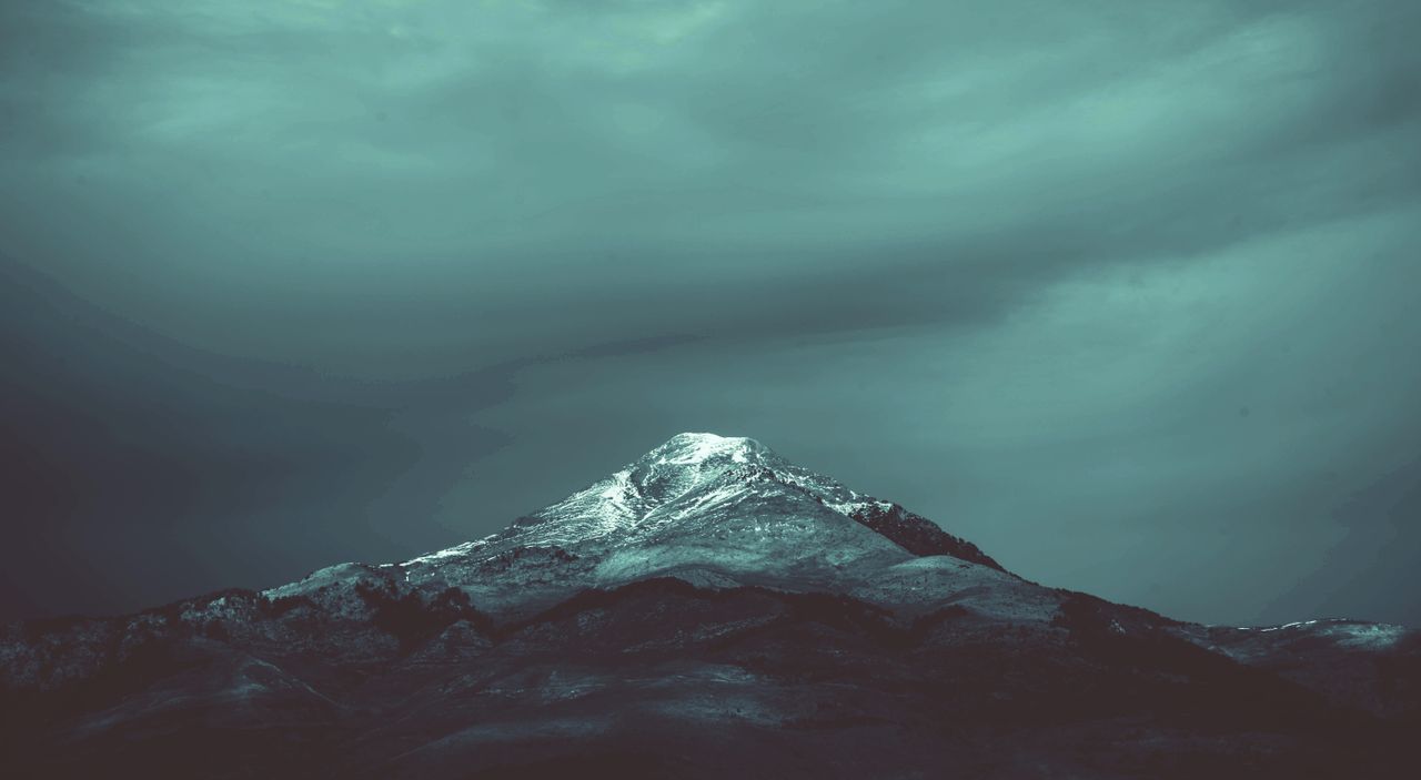 a dramatic snow capped mountain peak in algeria set against a moody sk