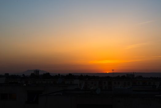 Captivating sunset over urban rooftops with vibrant orange and yellow hues, creating a serene silhouette of the skyline.