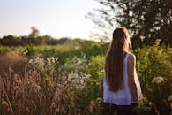 一名长发女子站在阳光明媚的乡间田野上，四周开满野花