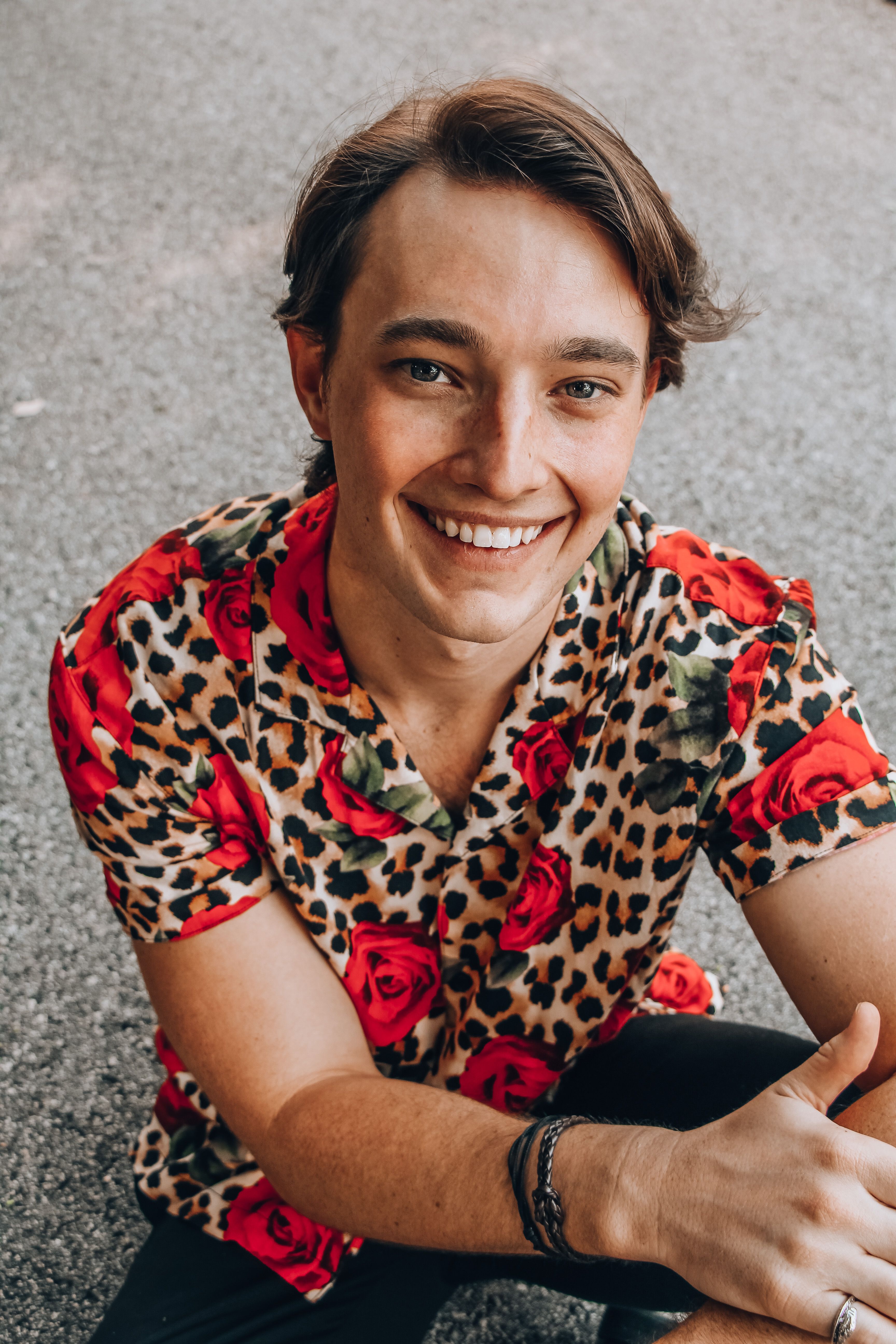 From above of young glad sincere male in stylish outfit with leopard ornament looking at camera on pavement